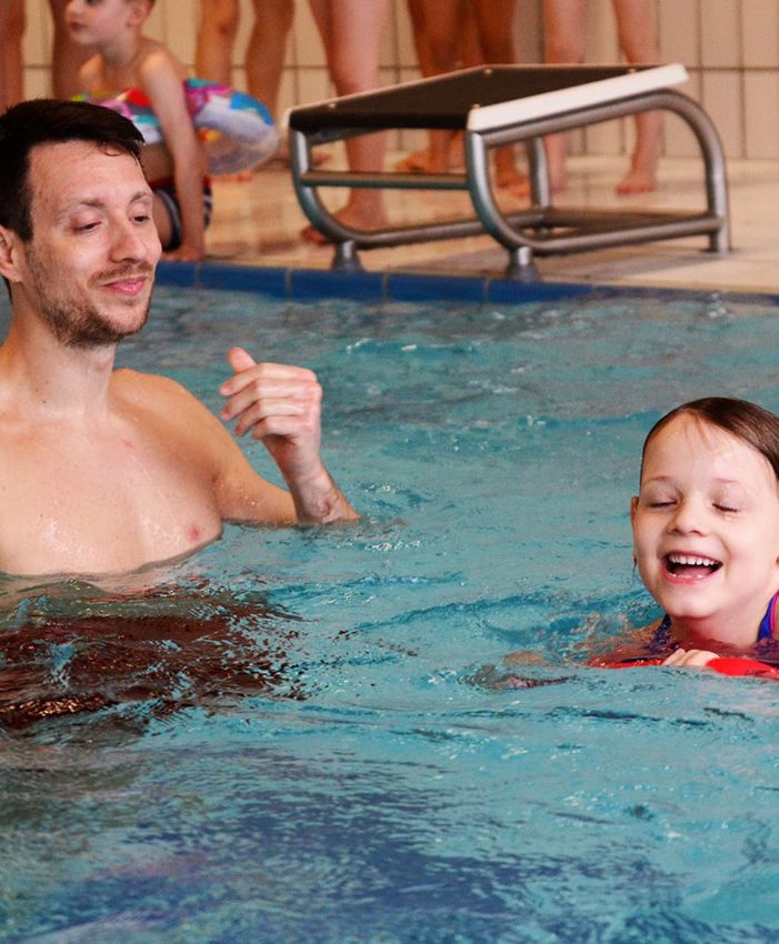 Marco Baldauf lacht mit einem Mädchen im Wasser