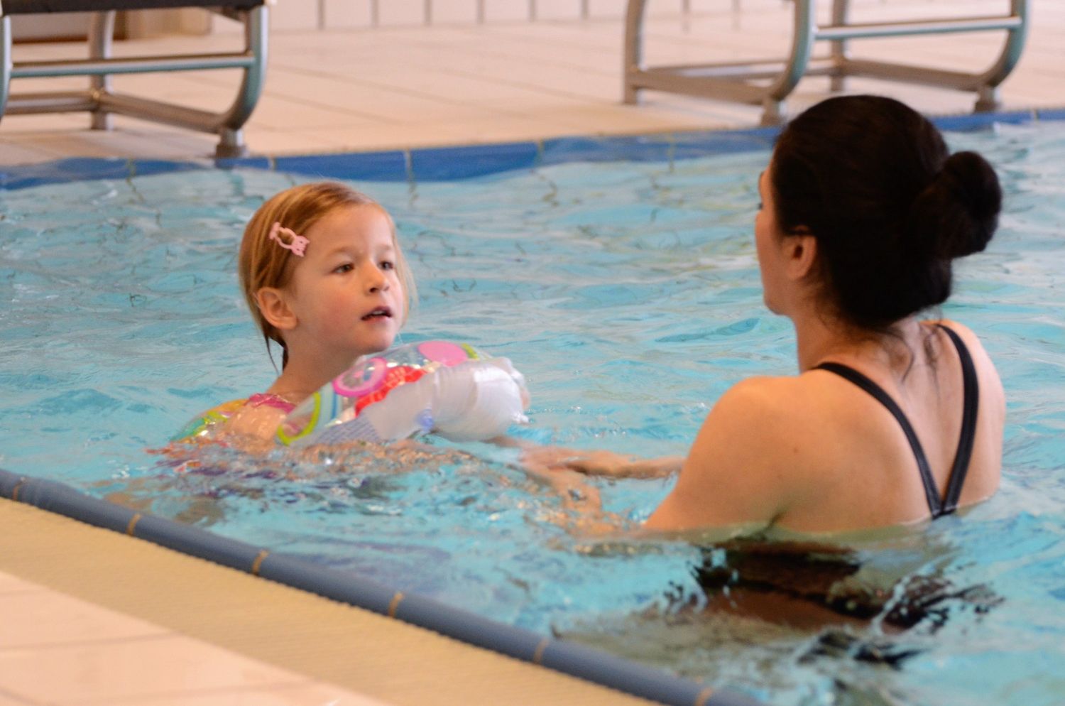 Mädchen mit Schwimmflügeln übt mit der Schwimmlehrerin